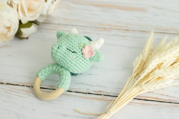 Hochet dragon vert en crochet avec une fleur rose sur l’oreille et anneau de dentition en bois. »